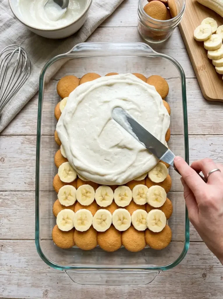 Layering vanilla wafers and fresh banana slices in a baking dish for banana pudding.