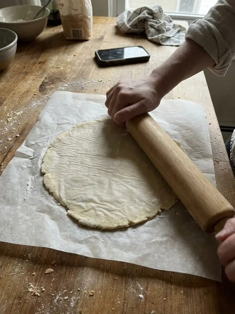 Rolling gluten free tortilla dough between two sheets of parchment paper on a wooden table
